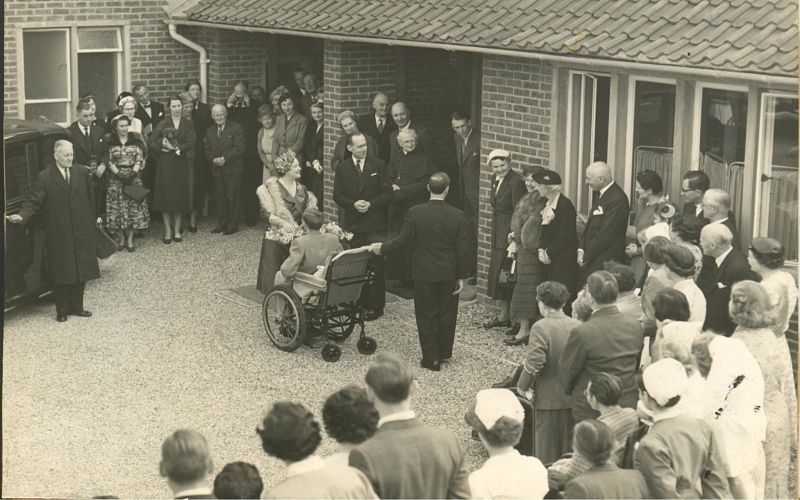 People watching the Queen Mother talking to a wheelchair-user, black and white photo