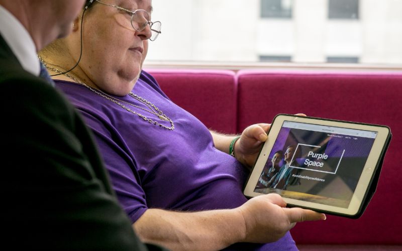 A woman in a purple shirt looking at the PurpleSpace website on a tablet