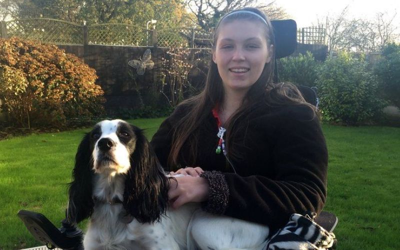 Lucy Watts in a wheelchair in a garden, with a dog on her lap