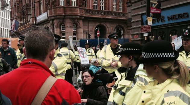 A wheelchair-user speaks into a microphone surrounded by police officers
