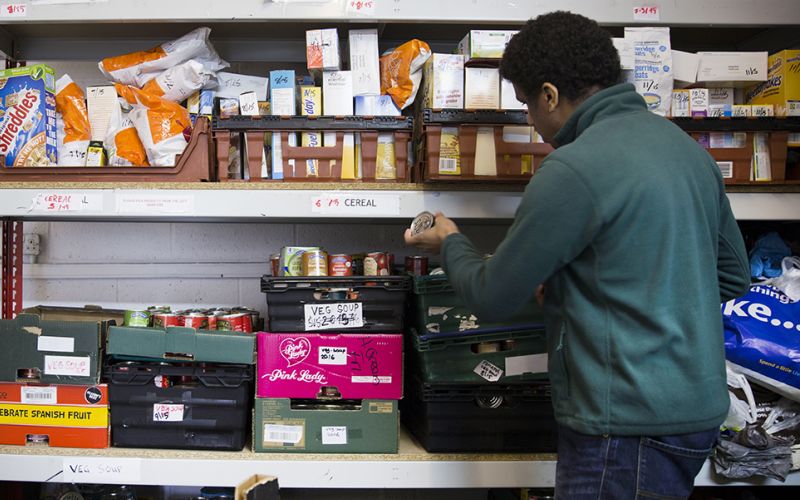 A man sorts shelves stacked with packets and tins of food
