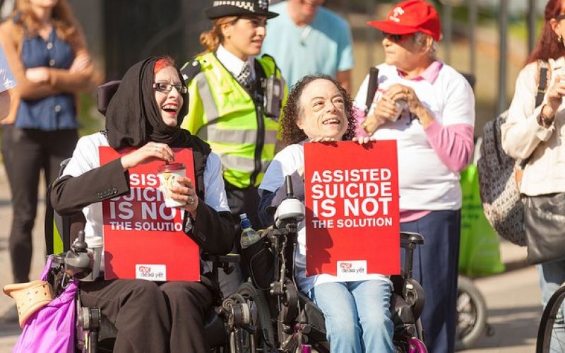 Two female wheelchair-users hold placards saying 'assisted suicide is not the solution'