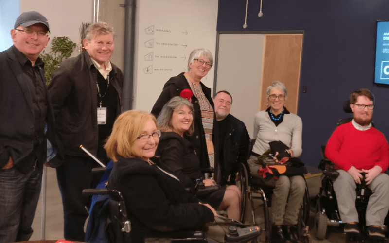 Eight people, including four wheelchair-users smiling at the camera