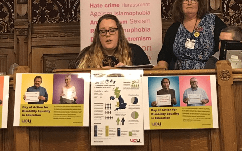 A woman speaks from a platform with campaigning pictures pinned to the table she is sitting at
