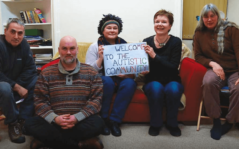 Five people hold a sign saying welcome to the autistic community