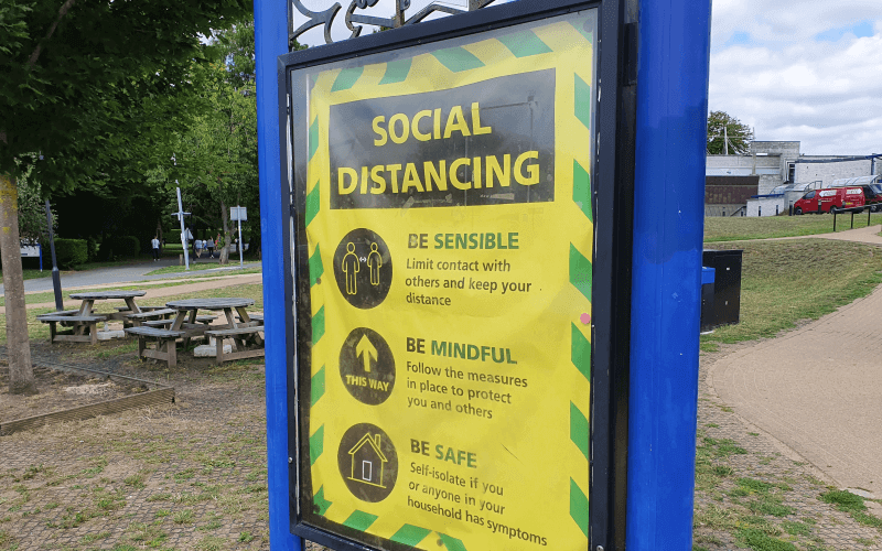 A yellow social distancing sign in a park