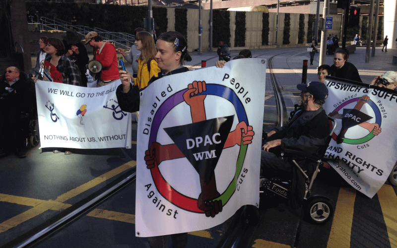 A dozen DPAC activists holding DPAC banners as they block a tram line
