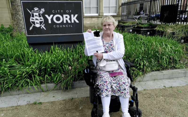 A female wheelchair-user holds up a letter in front of a City of York Council sign