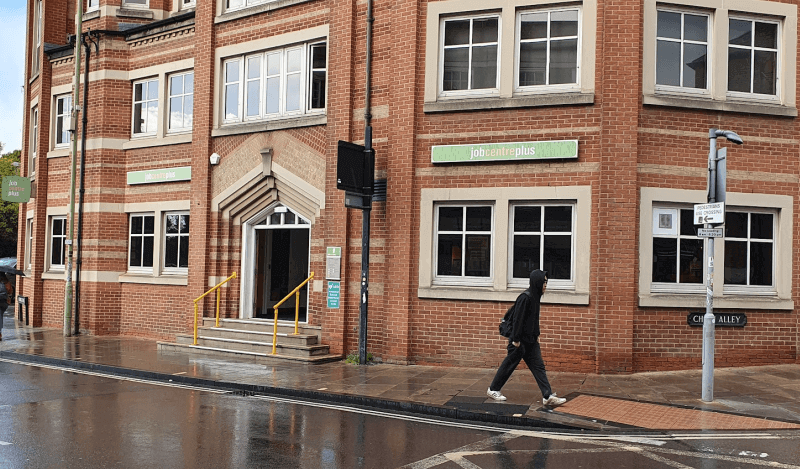 A large red brick building with three storeys and four steps to the entrance and green signs for jobcentreplus