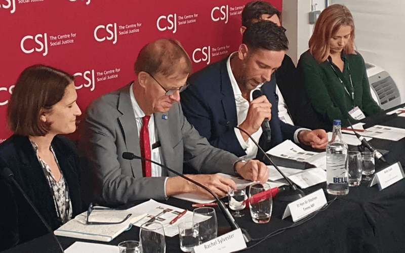 Sir Stephen Timms looking at his notes as he sits on a panel flanked by two women and two men, with a board advertising The Centre for Social Justice behind them