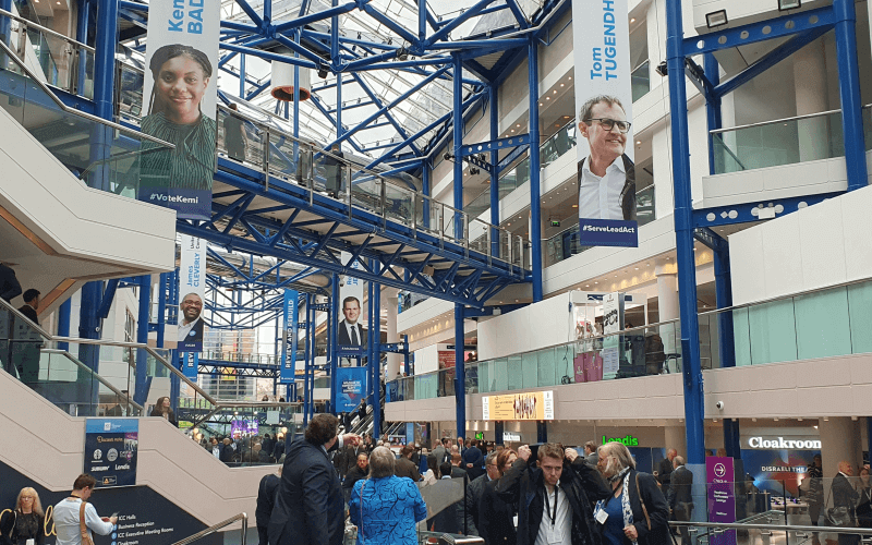 Huge vertical banners showing the four candidates for party leader hanging from a glass roof above people milling about at the Conservative conference