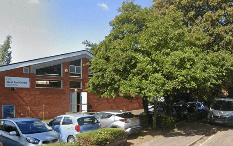 Cars parked beside a tree in front of a red brick building with an open door.