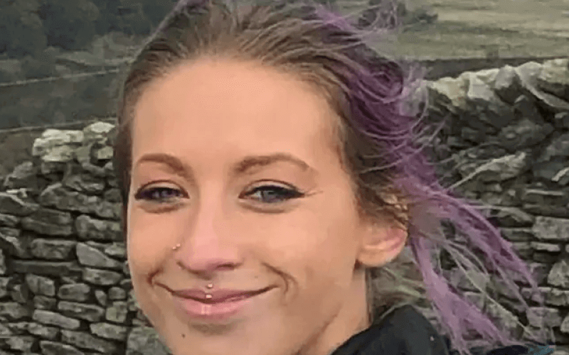 Head and shoulders of Krissi Hunt, smiling, in front of a dry stone wall