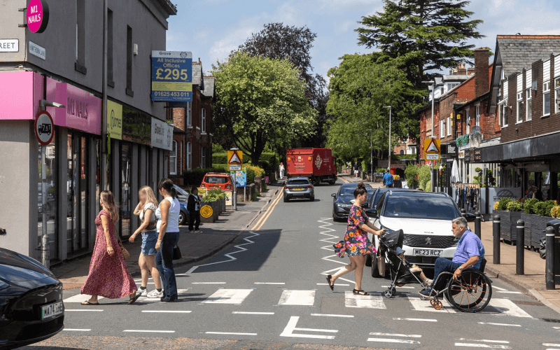 A wheelchair-user starts to cross a side road where there are striped black and white markings across the road